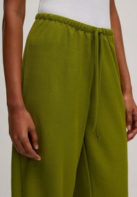 Groene, wijde broek met een textuurstof, voorzien van een elastische tailleband en een trekkoord. Gedetailleerde stiksels zichtbaar nabij de taille.