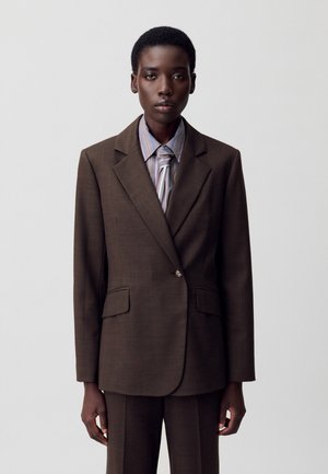 Blazer marron ajusté avec deux poches avant, revers crantés et une fermeture à un bouton, associé à une chemise rayée et un pantalon coordonné.