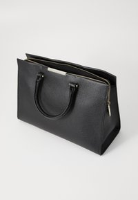 Sac fourre-tout en cuir noir avec une finition texturée, deux poignées courtes, une fermeture éclair et un accent métallique à l'avant.