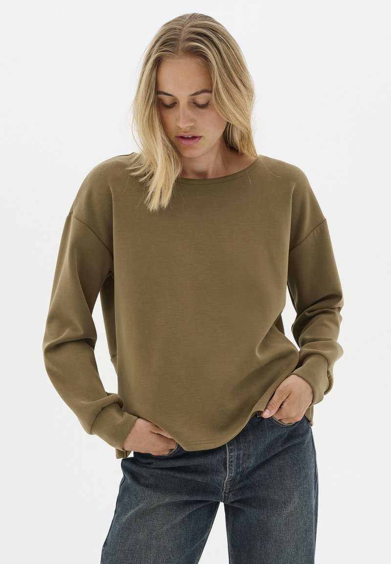 Felpa khaki con maniche lunghe, polsini a coste e scollatura rotonda, abbinata a jeans in denim blu scuro. Texture del tessuto liscia.