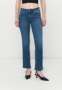 Blå denim jeans med en tettsittende midje, rett ben-design og fliserte hem. Brukt med svarte spisse slingback-hæler.