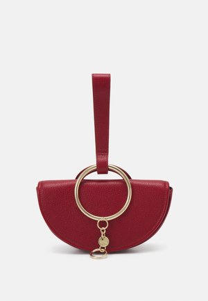 Petite pochette en cuir rouge en forme de demi-lune avec anneau en métal doré et petit pendentif suspendu sur fond blanc.