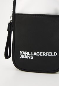 Fekete nylon tok sima textúrával, cipzáras záródással, elől fehér logó felirattal: "KARL LAGERFELD JEANS".