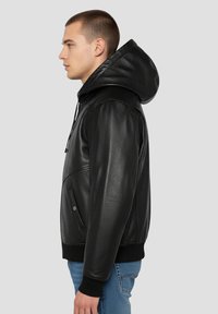 Veste en cuir noir avec capuche, dotée d'une fermeture éclair, de poches latérales et de poignets côtelés. Texture lisse et coupe ajustée.