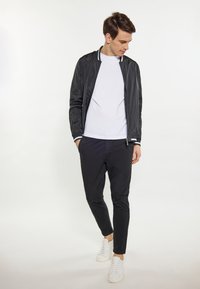 Giacca bomber leggera nera con strisce bianche, indossata sopra una maglietta bianca semplice, abbinata a pantaloni neri e sneaker bianche.