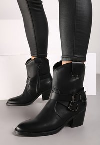 Bottines en cuir noir avec une fermeture éclair sur le côté, dotées de deux sangles et boucles, orteil carré et un petit talon épais.
