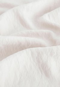Bílá texturovaná látka s jemným, zmačkaným povrchem. Světlý a vzdušný vzhled s mírným leskem, který vytváří jemný, nenápadný dojem.