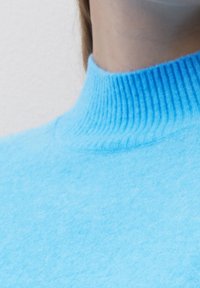 Pull à col roulé bleu clair avec un col côtelé et une texture douce, raccourci pour dévoiler la partie supérieure de la poitrine.