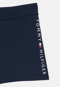 Μπλε ναυτικό σορτς κολύμβησης με μαλακή μέση, τυπωμένο κείμενο "TOMMY HILFIGER" και μικρή λεπτομέρεια λογότυπου σε κόκκινο, άσπρο και μπλε στη πλευρά.