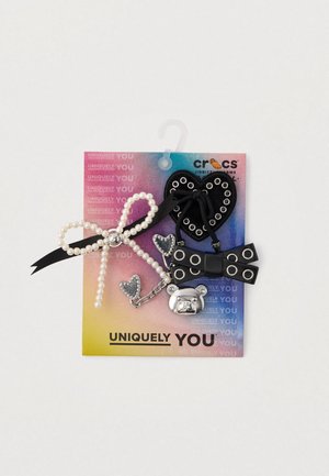 Black rubber heart-shaped charm with eyelets, silver bear charm, pearl-accented bow, and a glittery heart on a colorful backing.