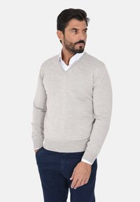 Maglione grigio chiaro a scollo a V realizzato in un tessuto morbido, con maniche lunghe e polsini a costine, abbinato a pantaloni blu navy.