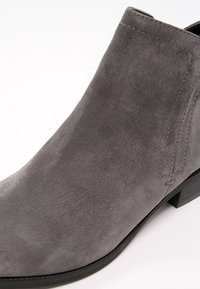 Botte de cheville en suede gris avec une texture lisse, petit talon empilé et un minimalisme de couture sur le côté pour un enfilage facile.