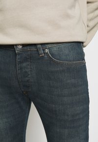 Jeans i denim med mörkblå tvätt, med slim fit, fem fickor och kontrasterande sömmar, samt en metallknappstängning i midjan.