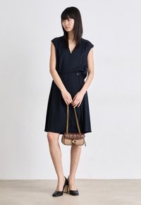 Black sleeveless dress with a v-neckline and belted waist, paired with a quilted brown handbag and black pointed-toe heels.