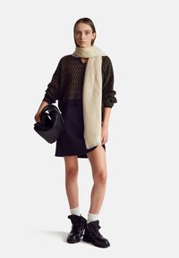 Sweter z dzianiny w czarno-zielony wzór, kremowy szalik, czarna torba, granatowa spódnica i czarne sznurowane botki z białymi skarpetkami. Prosty design, teksturowany.