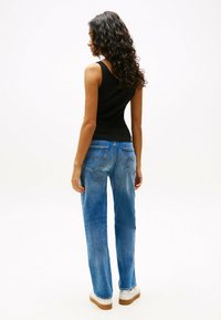 Top aderente nero, jeans dritti blu, sneaker piatta bianche, vista posteriore che evidenzia tasche e texture del denim.
