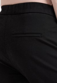Schwarze Hose aus glattem Stoff, mit einer einzigen Gesäßtasche ohne sichtbare Hardware und mittelhoher Taille.