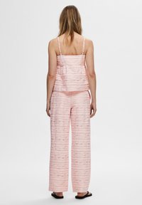 Svetloružový dvojdielny outfit s textúrovaným, vrstveným topom na tenkých ramienkach a nohavicami s širokými nohavicami v podobnom vzore. Súčasťou sú aj ploché sandále.