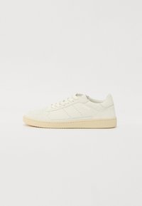 Hvitt lær sneakers med teksturert overflate, beige såle, perforerte detaljer på tåen og subtil merking på siden.
