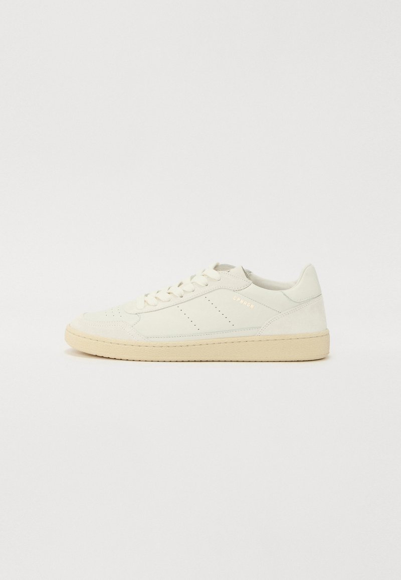 Hvitt lær sneakers med teksturert overflate, beige såle, perforerte detaljer på tåen og subtil merking på siden.