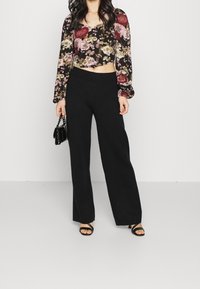 Pantaloni neri a vita alta abbinati a un top corto floreale a maniche lunghe, con maniche a sbuffo e un mix di fiori rosa e viola.