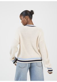 Maglione lavorato a maglia di colore crema con una vestibilità ampia, caratterizzato da polsini e orlo a righe blu e navy. Il retro presenta un motivo testurizzato e una finitura a costine.