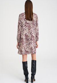 Květinové šaty v světle fialové barvě s dlouhými rukávy, sklady a volným střihem; nošeny s vysokými černými koženými botami.