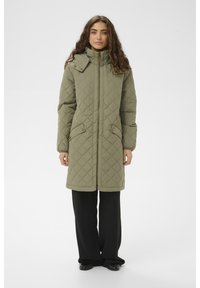 Olīvu zaļš pārklāts garš mētelis ar augstu apkakli, sānu kabatām un priekšējo rāvējslēdzēju. Izgatavots no mīksta, polsterēta materiāla.