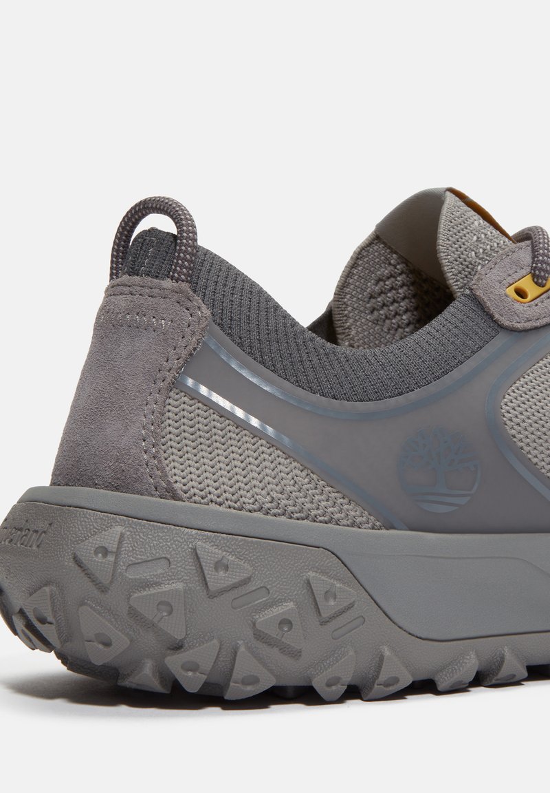 Zapatilla deportiva gris con parte superior de malla y detalles en ante, suela de goma texturizada y un logo en el lateral.