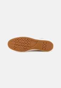 Gummisåle til sneakers med en teksturert diamantmønster i brun. Hvit mellomsåle med røde aksenter, rund tådesign og glatte kanter.