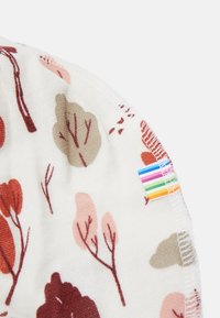 Tecido de malha com um fundo branco apresenta um padrão de árvores estilizadas em tons de vermelho, rosa e bege. Inclui uma etiqueta arco-íris.