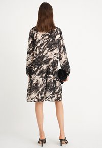 Robe à motif abstrait noir et crème avec des manches longues et une jupe à volants. Tissu transparent, associée à une pochette noire et des talons ouverts.