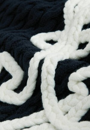 Tmavomodrá a biela pletená deka s výrazným hrubým vrkočovým vzorom a mäkkou, textúrovanou priadzou. Dizajn zdôrazňuje kontrastné farby a textúru.