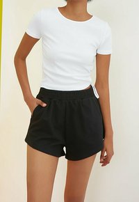 Haut blanc à manches courtes en côte, associé à un short noir à taille élastique. La tenue présente une coupe décontractée et un tissu lisse et léger.