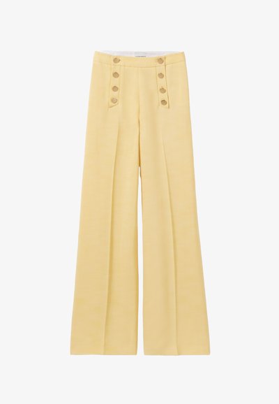 Pantalon large jaune en tissu lisse. Présente des boutons décoratifs à la taille et des plis sur le devant pour plus de dimension.