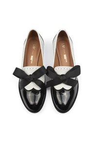 Mustvalge patendinahast loafers, millel on tekstureeritud pealis, suur must siidist lips ja laineline äärise detail.