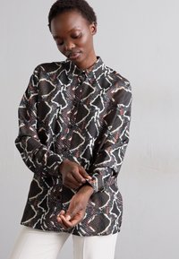 Camicia a maniche lunghe con motivo a serpente, caratterizzata da colori nero, bianco e rosso, colletto button-down e tessuto dalla texture liscia.