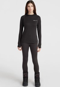 Black long-sleeve top and leggings, made of smooth, stretchy fabric. Accented by a small white logo on the chest. Paired with black winter boots.