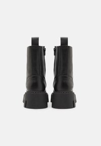 Bottines en cuir noir avec une semelle en caoutchouc épaisse, fermetures éclair sur les côtés et deux languettes à l'arrière, présentant une texture lisse et un design simple.