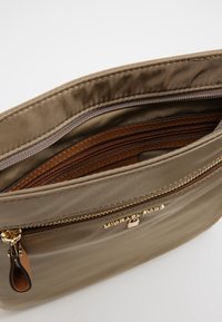Olivengrøn satin taske med guldfarvet hardware, der har lynlåslukning og flere indvendige rum i brunt struktureret materiale.