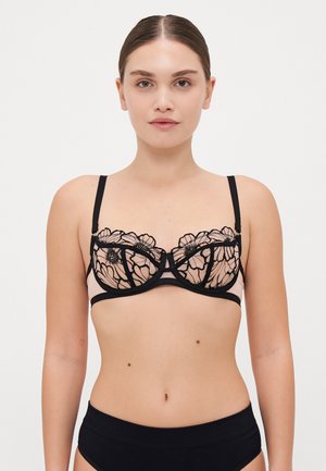 Svart blomstret blonde-bh med en gjennomsiktig nude-panel, underwire-støtte, justerbare stropper og en sentrum-bue detalj. Designet for kontrast og eleganse.