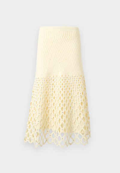Jupe tricotée couleur crème avec une partie supérieure ajustée et un motif ajouré en losanges sur la partie inférieure évasée, ourlet festonné.