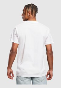 Hvid bomulds t-shirt med en afslappet pasform, korte ærmer og et ensfarvet design, set fra ryggen mod en grå baggrund.