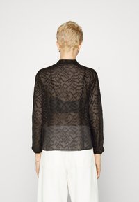 Blusa nera trasparente con maniche lunghe e dettagli di perline intricati. Presenta un colletto, un tessuto testurizzato e una vestibilità leggermente ampia.