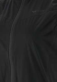 Svart zip-up jacka tillverkad av mjukt tyg med lätt vikt. Har en logo på bröstet och sömnadsdetaljer längs dragkedjan.