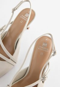 Beige kožené sandály s nízkým podpatkem, s nastavitelným páskem kolem kotníku a designem se strappy. Uvnitř je na podrážce embosováno logo "FOREVER COMFORT".