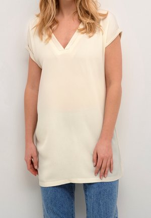 Haut crème à manches courtes avec un décolleté en V, fabriqué en tissu texturé, associé à un jean bleu clair.