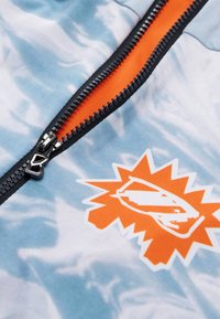 Jakke med lynlås i blåt tie-dye mønster, med en orange lynlås og grafisk logo i orange og hvid på forsiden.