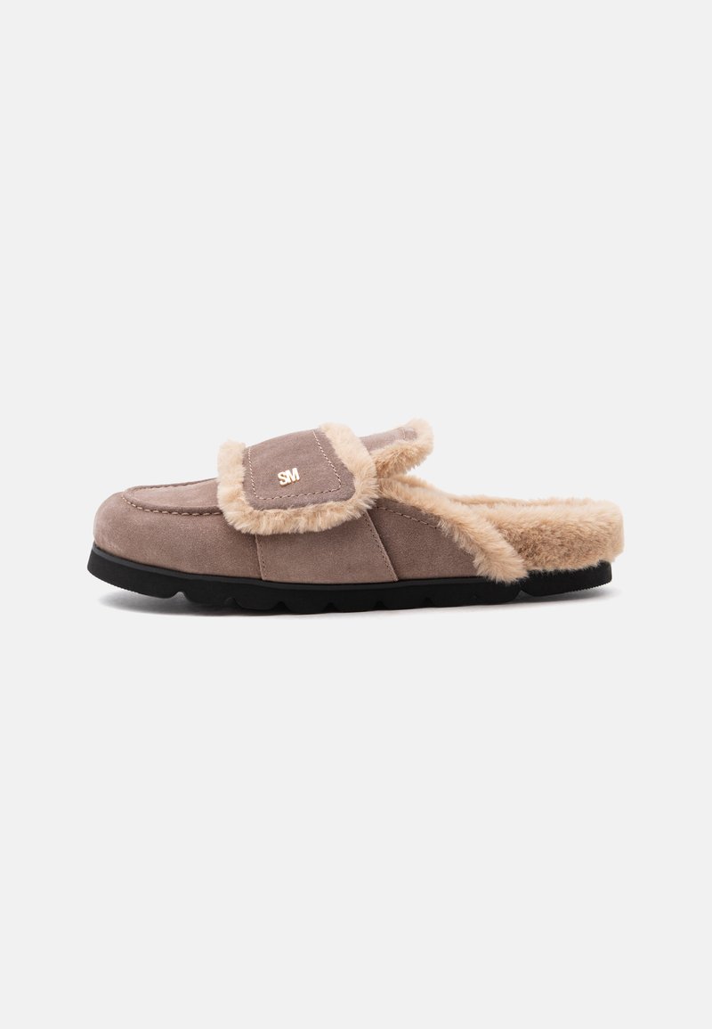 Chausson marron en daim à enfiler avec bordure et doublure en fourrure beige, semelle noire, et petit logo doré "SM" sur la languette supérieure.