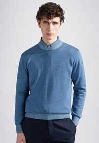 Maglione blu a maglia con colletto e polsini a coste. Presenta un design con mezza zip e una silhouette aderente, abbinato a pantaloni scuri.